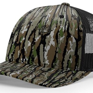 May include: A camouflage baseball cap with a black mesh back. The cap features a pattern of green, brown, and white, with a small logo on the front. The brim is curved and the cap has a button on top.