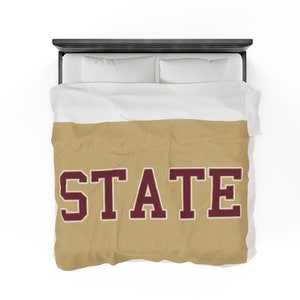 May include: A gold and maroon duvet cover with the word "STATE" printed in large maroon letters.