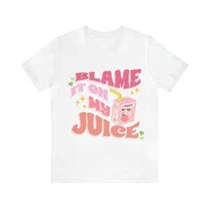 May include: White t-shirt with a pink and white graphic that says "Blame it on my juice" with a cartoon peach juice box.