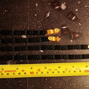 May include: Four black and gold decorative strips with a yellow Stanley tape measure. The tape measure shows measurements in centimetres. The strips have gold accents and are arranged parallel to each other.