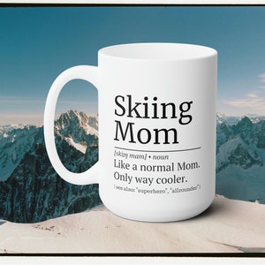 May include: White ceramic coffee mug with a black graphic that says "Skiing Mom" and defines the term as "Like a normal Mom. Only way cooler."  The mug is sitting on a snowy mountaintop.