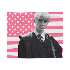 May include: A blanket featuring a black and white image of a person in a formal outfit, set against a pink American flag background. The flag has white stars and pink stripes.