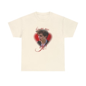 May include: A cream-coloured t-shirt with a portrait inside a red heart. The portrait is of a person with dark hair. The text "it's no use, To!" is written in red script above and below the portrait.