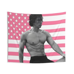 May include: A black and white tapestry featuring a muscular person posing in front of a pink and white American flag. The person is wearing black shorts and glasses. The flag has pink stripes and white stars.