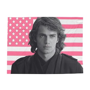 Peut inclure: Une photo en noir et blanc d'un homme aux cheveux longs, portant une chemise noire, sur un fond rayé rose et blanc. L'arrière-plan ressemble à un drapeau américain.