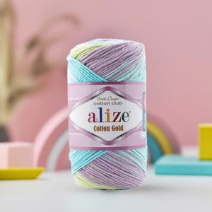 May include: A colorful skein of Alize Cotton Gold yarn. The yarn is a blend of pastel colors, including blue, purple, yellow, and green. The label features the brand name and product details. Ideal for knitting and crochet projects.