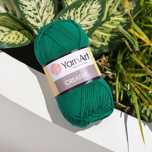 以下が含まれることがあります： 緑色のYarnArt Creativeの毛糸玉。ラベルにはYarnArtのロゴと「CREATIVE」の文字が記載されています。毛糸は鮮やかな緑色で、さまざまな編み物やかぎ針編みのプロジェクトに最適です。画像は緑の葉を背景にしています。