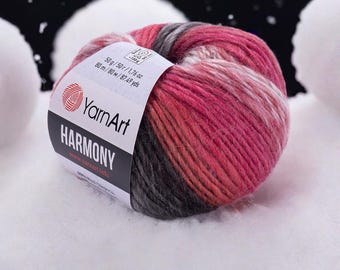 May include: A ball of YarnArt HARMONY yarn in shades of pink, red, grey, and white. The label indicates 50g/1.76 oz and 80 m/87.49 yds. The yarn is set against a white, snowy background.