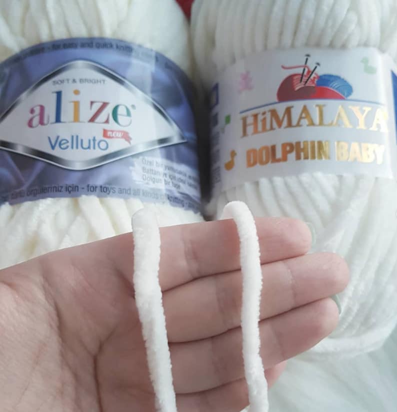 Puede incluir: Dos ovillos de hilo blanco, uno etiquetado como "alize Velluto" y el otro como "HIMALAYA DOLPHIN BABY". El hilo es suave y esponjoso, perfecto para tejer o hacer ganchillo.