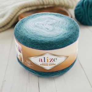Könnte beinhalten: Eine Kugel aus teal- und weißfarbenem Ombre-Garn mit dem Etikett "Alize Angora Gold Ombre Batik". Das Garn hat eine weiche, flauschige Textur, ideal zum Stricken oder Häkeln. Das Garn ist eine Mischung aus Farben.