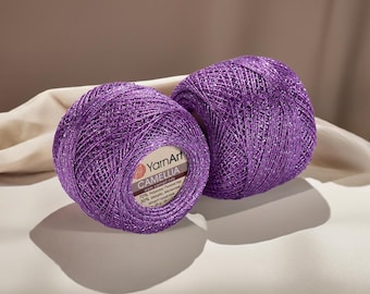 Op de afbeelding: Twee paarse garenbollen met een metallic glans. Op één bol staat "YarnArt CAMELLIA". Het garen is een mix van polyester en metallic vezels. Elke bol weegt ongeveer 20 gram, perfect voor brei- en haakprojecten.