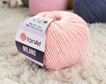 May include: A ball of light pink YarnArt Milano yarn. The label indicates 50g / 1.76 oz and 130 m / 142.17 yds. Other balls of yarn in various colors are visible in the background.