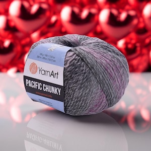 Può includere: Gomitolo di filato YarnArt Pacific Chunky, sfumature di grigio e rosa. L'etichetta indica 100 g e 200 m. Adatto per progetti di maglia e uncinetto. Sfondo con decorazioni rosse sfocate a forma di cuore.