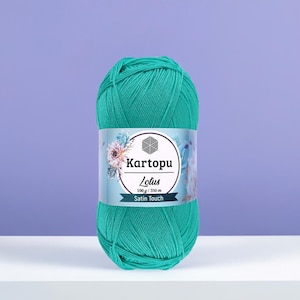 以下が含まれることがあります： 「Kartopu Lotus Satin Touch」と書かれたラベルが付いた、ティール色の毛糸玉。ラベルには花の模様と「100 g / 350 m」の文字が入っています。紫色の背景に毛糸が展示されています。