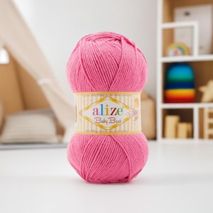 May include: A ball of bright pink Alize Baby Best yarn. The yarn is wrapped with a label that reads "alize Baby Best" in gold and white. The yarn is a soft, textured material, perfect for knitting or crocheting baby items.