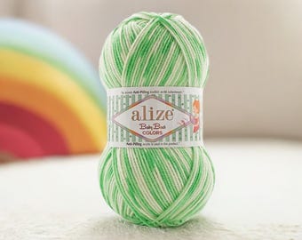 Puede incluir: Una madeja de hilo a rayas verdes y blancas con una etiqueta que dice "alize Baby Best COLORS". El hilo es de color verde claro con rayas blancas. La etiqueta tiene forma de diamante con el nombre de la marca y una imagen de dibujos animados.