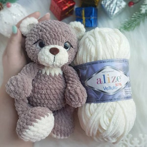 Puede incluir: Un oso de peluche tejido a crochet con un esquema de color marr&oacute;n y blanco. El oso est&aacute; sentado junto a una bola de hilo blanco con una etiqueta que dice "alize Velluto".