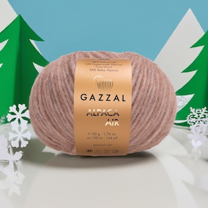May include: A ball of Gazzal Alpaca Air yarn in a soft, muted pink color. The label indicates the yarn is made of 28% Polyamide, 14% Superwash Merino Fine Wool, and 58% Baby Alpaca. The ball weighs 1.76 oz and is approximately 164 yards long.