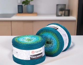 May include: Two skeins of YarnArt Flowers Moonlight yarn. The yarn is a gradient of teal, blue, and green. The label reads "YarnArt Flowers Moonlight". The yarn is on a white surface.