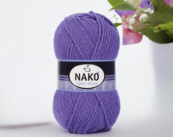 May include: A ball of purple Nako Sport Wool yarn. The yarn is wrapped with a black and white label that reads "NAKO Sport Wool". The yarn is a solid, vibrant purple colour. The background is a soft white with a bouquet of flowers.