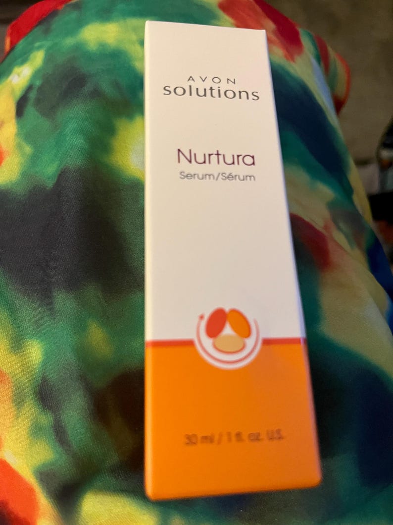 May include: A rectangular white and orange cardboard box for Avon Solutions Nurtura Serum. The front features the text AVON solutions Nurtura Serum/S&eacute;rum and a circular graphic with three colored shapes. The bottom indicates 30 ml / 1 fl. oz. U.S.