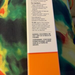 May include: A rectangular white skincare product box with an orange base. The front panel features black text detailing ingredients like snow mushroom extract, panthenol, sunflower seed oil, and hyaluronic acid, along with usage instructions and warnings.
