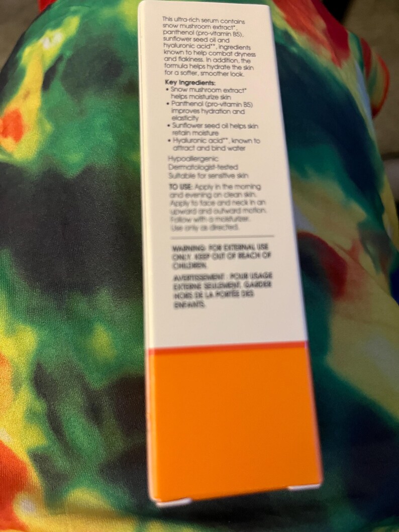 May include: A rectangular white skincare product box with an orange base. The front panel features black text detailing ingredients like snow mushroom extract, panthenol, sunflower seed oil, and hyaluronic acid, along with usage instructions and warnings.