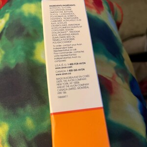 May include: A rectangular white product box with a bright orange base. The box features black printed text listing ingredients including water, glycerin, and sodium hyaluronate, along with contact information for Avon in the USA and Canada.