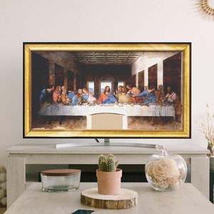 May include: A living room interior with a large framed painting of The Last Supper hanging above a modern TV stand. The painting is in a gold frame and the TV stand is made of wood. There are two white stools in front of the TV stand and a coffee table with a vase of flowers and a potted cactus on it.