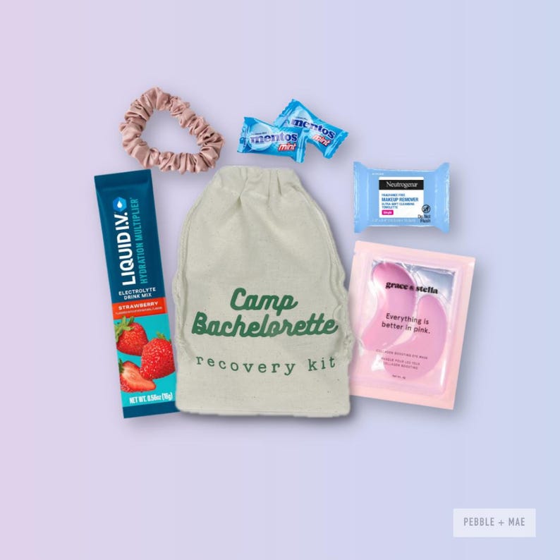 May include: A white drawstring bag with the text "Camp Bachelorette recovery kit" printed on it. The bag is surrounded by various items, including a pink hair tie, a blue electrolyte drink mix packet, a pink eye mask, a blue makeup remover wipe, and two blue mints.