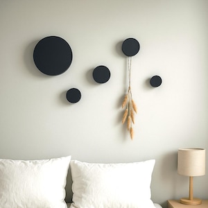 Op de afbeelding: Een slaapkamer met een bed met witte lakens en kussens. Boven het bed zijn verschillende zwarte cirkelvormige wanddecoraties. Rechts staat een kleine houten nachtkast met een lamp.