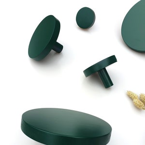 May include: A collection of dark green wooden cabinet knobs and pulls in various sizes. The knobs have a flat, circular design with a cylindrical stem. The hardware is arranged on a white background, showcasing the modern design.