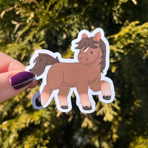 May include: A brown and white cartoon horse sticker with a sad expression. The sticker is on a white background and has a white outline.