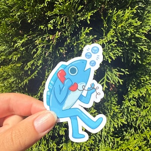 May include: A blue sticker featuring a cartoon fish holding a red telephone receiver. The fish has a white belly and is surrounded by bubbles. The sticker is held against a backdrop of green foliage.