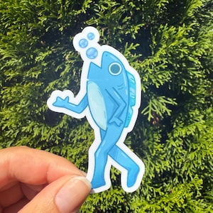 May include: A blue sticker featuring a cartoon fish with legs, walking and blowing bubbles. The fish has a light blue belly and a dark blue outline. The sticker is held against a background of green foliage.
