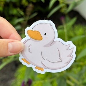 May include: A white duck sticker with a yellow beak and orange feet. The duck has a cartoonish style and is looking to the left.