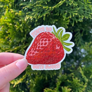 May include: A white sticker with a red strawberry illustration and the text "You're so berry sweet!" in pink lettering.