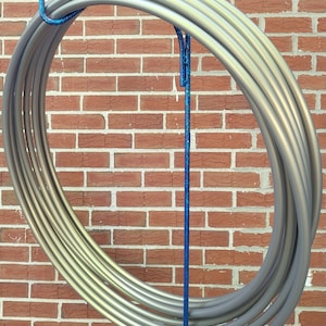 May include: A set of six silver hoop dance hoops stacked and hanging on a blue glitter stand against a brick wall.