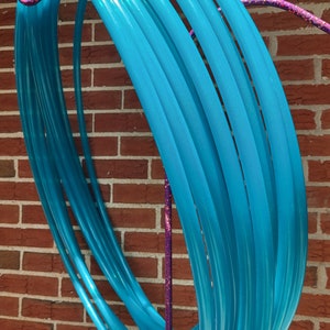 May include: A set of turquoise blue plastic hula hoops stacked on a purple stand. The hoops are shiny and have a slight iridescent shimmer.