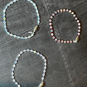 Könnte beinhalten: Drei Kristall-Armbänder mit Magnetverschlüssen. Die Armbänder bestehen aus kleinen, facettierten Perlen in den Farben Blau, Rot und Klar.