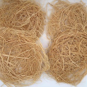 May include: Close-up of several bundles of natural, light brown nesting material. The material appears to be made of dried plant fibers, tightly woven into round shapes. The texture is rough and fibrous, suitable for birds.