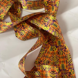 May include: A roll of decorative ribbon with a vibrant, geometric pattern in shades of orange, yellow, green, and purple. The ribbon is unspooled, revealing its intricate design. The ribbon is likely used for crafts, gift wrapping, or other decorative purposes.