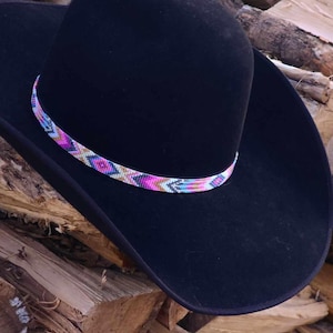 May include: A black cowboy hat with a colorful beaded band. The band features pink, blue, white, and brown beads in a geometric pattern.
