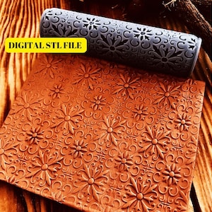 May include: A grey rolling pin with a floral design. The rolling pin is used to create an embossed pattern on a surface. The surface is a brown clay-like material with a floral design.