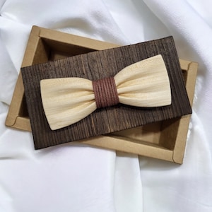 Könnte beinhalten: Ein braunes Holz-Fliege mit einem braunen Lederband, in einer dunkelbraunen Holzkiste mit einem hellbraunen Pappdeckel.