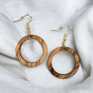 Könnte beinhalten: Ein Paar runde Holzohrringe mit goldenen Haken. Die Ohrringe sind aus hellbraunem Holz mit natürlicher Maserung.