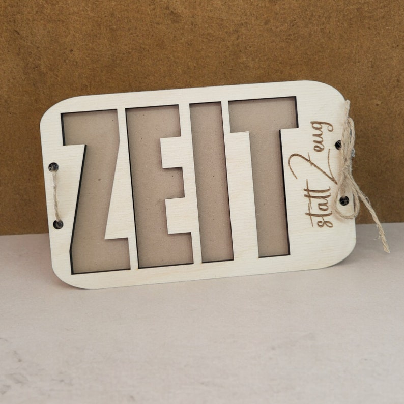 May include: A wooden sign with the word "ZEIT" cut out and the phrase "statt Zeug" written below it. The sign is attached to a piece of twine.