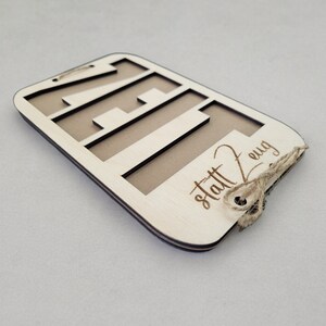 May include: A wooden sign with the number 21 cut out and the text "statt 2 ewg" engraved on the bottom. The sign is tied with twine.