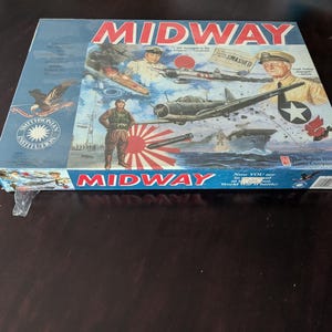 May include: A rectangular board game box titled MIDWAY featuring a colourful illustration of World War II naval and aerial combat. The artwork includes military personnel, fighter planes, a ship, a red sun emblem, and the Smithsonian Institution logo.