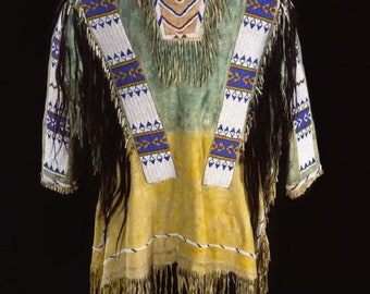 May include: A Native American buckskin shirt with a green and yellow body. The shirt features white beaded straps with blue and gold geometric designs. Black fringe adorns the sleeves and hem. The yoke has a beaded design with fringe.